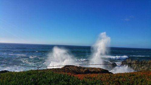 Scenic view of  crashing wave and  sea against clear blue sky