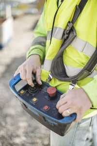 Midsection of construction worker operating control tool at site