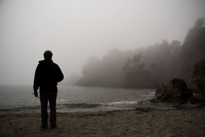 Rear view of man looking at sea during foggy weather