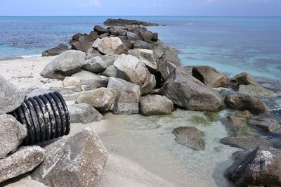 Rocks on shore at beach against sky