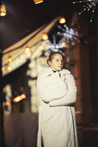 Woman wearing warm clothing while standing in city at nigh