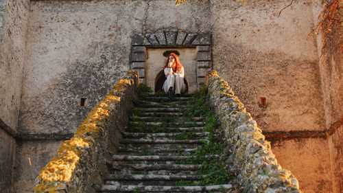 Beautiful girl with white dress sitting on the main entrance stairs of castle