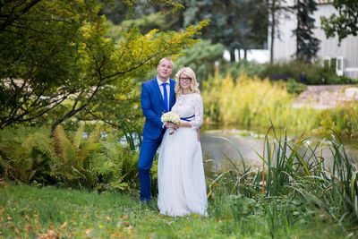 Portrait of newlywed couple standing by pond at park