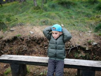 Cute boy with hands behind head looking away in forest