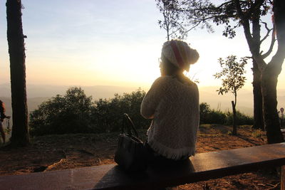 Rear view of woman sitting on rock against sky