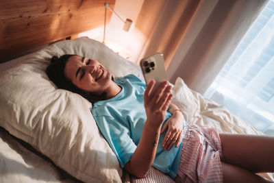 Young woman using mobile phone while lying on bed at home