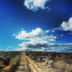 Road passing through field against cloudy sky