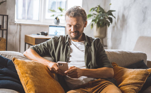 Young man using mobile phone while sitting at home