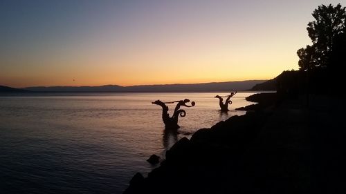 Silhouette birds on sea against clear sky during sunset