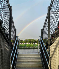 A stairway climbing upwards with a vibrant rainbow in the background.