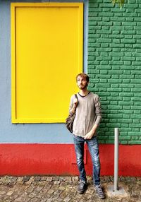 Portrait of smiling young man standing against yellow wall