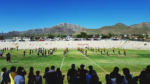 People on field by mountains against clear blue sky