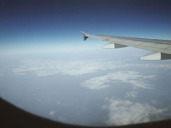 Aerial view of airplane wing over landscape against blue sky