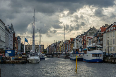 Boats in canal amidst buildings against cloudy sky during sunset
