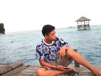 Man sitting by sea against clear sky