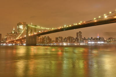 Illuminated bridge over river with city in background at night