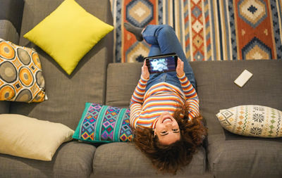 High angle portrait of smiling woman using digital tablet on sofa