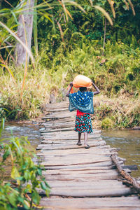 Rear view of young woman walking on footpath bridge carrying a sack of rice in the morning 