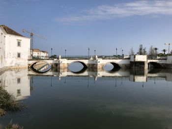 Bridge over river by buildings against sky