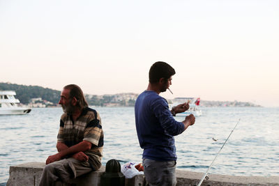 Friends sitting on sea shore against clear sky