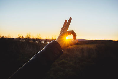 Optical illusion of person gesturing over sun during sunset