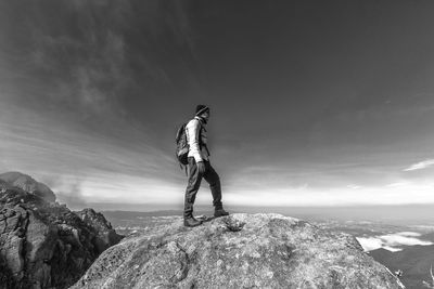 Side view of man standing on rock at mountain against sky