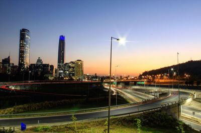 Light trails on street amidst buildings against sky during sunset