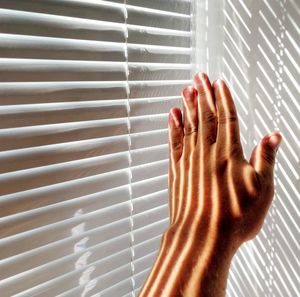 Cropped hand of person by blinds and wall