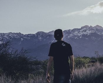 Rear view of man looking at mountains against sky