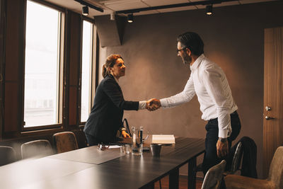 Mid adult lawyer shaking hands with mature client at board room in law office