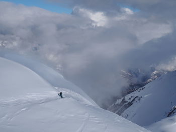 Mid distant view of person skiing on snow covered mountain against cloudy sky