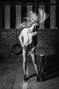 Smiling young woman tossing hair on footpath at night