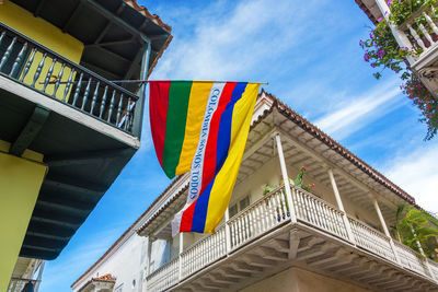 Low angle view of colorful flag with text on balcony against sky