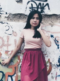 Portrait of young woman standing against wall