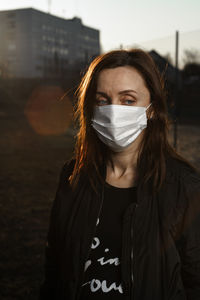 Portrait of beautiful young woman in mask standing outdoors 