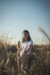 Portrait of smiling young woman standing on field against sky