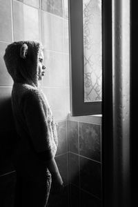 Side view of girl looking through window at home