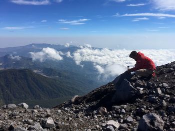 Woman crouching while arranging monopod on scenic mountain range against sky