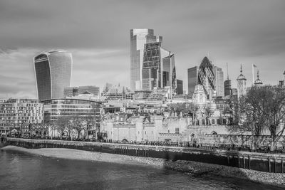 Modern buildings by river against sky in city