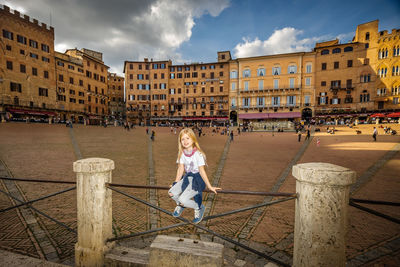 Girl sitting on railing in historical city against sky, piazza del campo in siena, tuscany italy