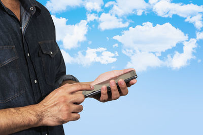 Midsection of man using smart phone while standing against blue sky