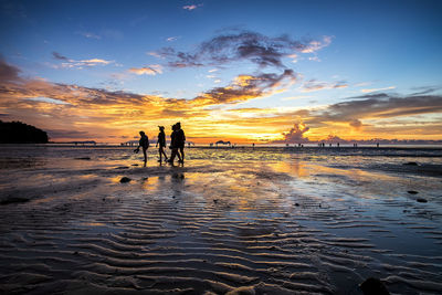 Silhouette people standing on beach against sky during sunset