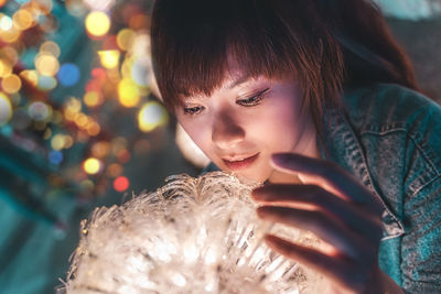 Close-up portrait of girl looking at illuminated christmas tree
