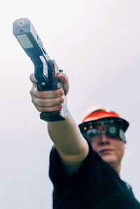 Low angle view of woman shooting with pistol against clear sky