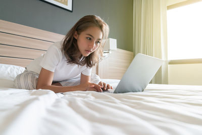 Young woman using laptop on bed at home