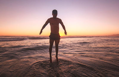 Doing exercises on the beach, jumping over the water under sunset light