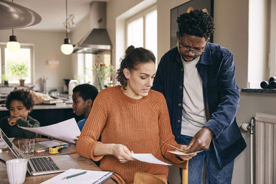 Multiracial couple discussing over financial bills while sons in background at home