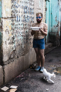 Full length of young man holding a bowl of water against wall