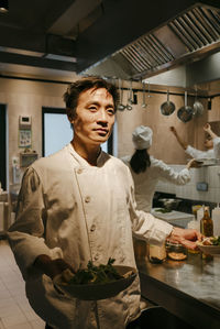 Male chef standing with salad bowl at illuminated commercial kitchen