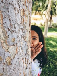 Close-up portrait of smiling young woman against tree trunk